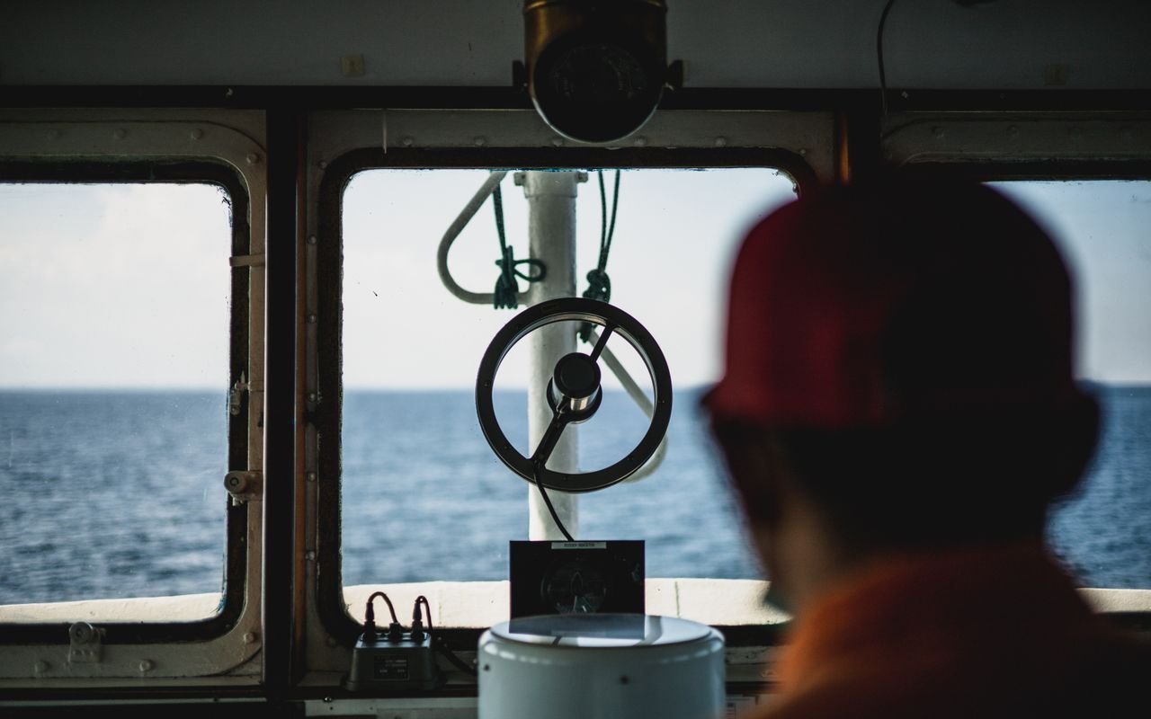 Looking through a ship's bridge window towards the ocean horizon.