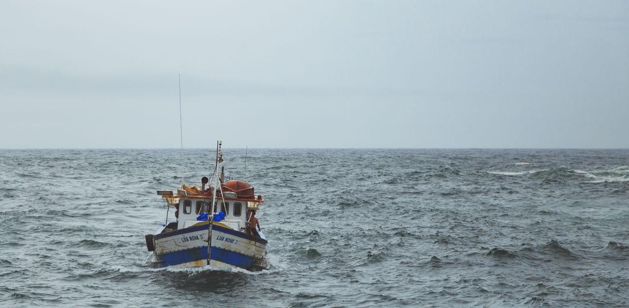 A lone fishing boat travels through the ocean waves under a cloudy sky.